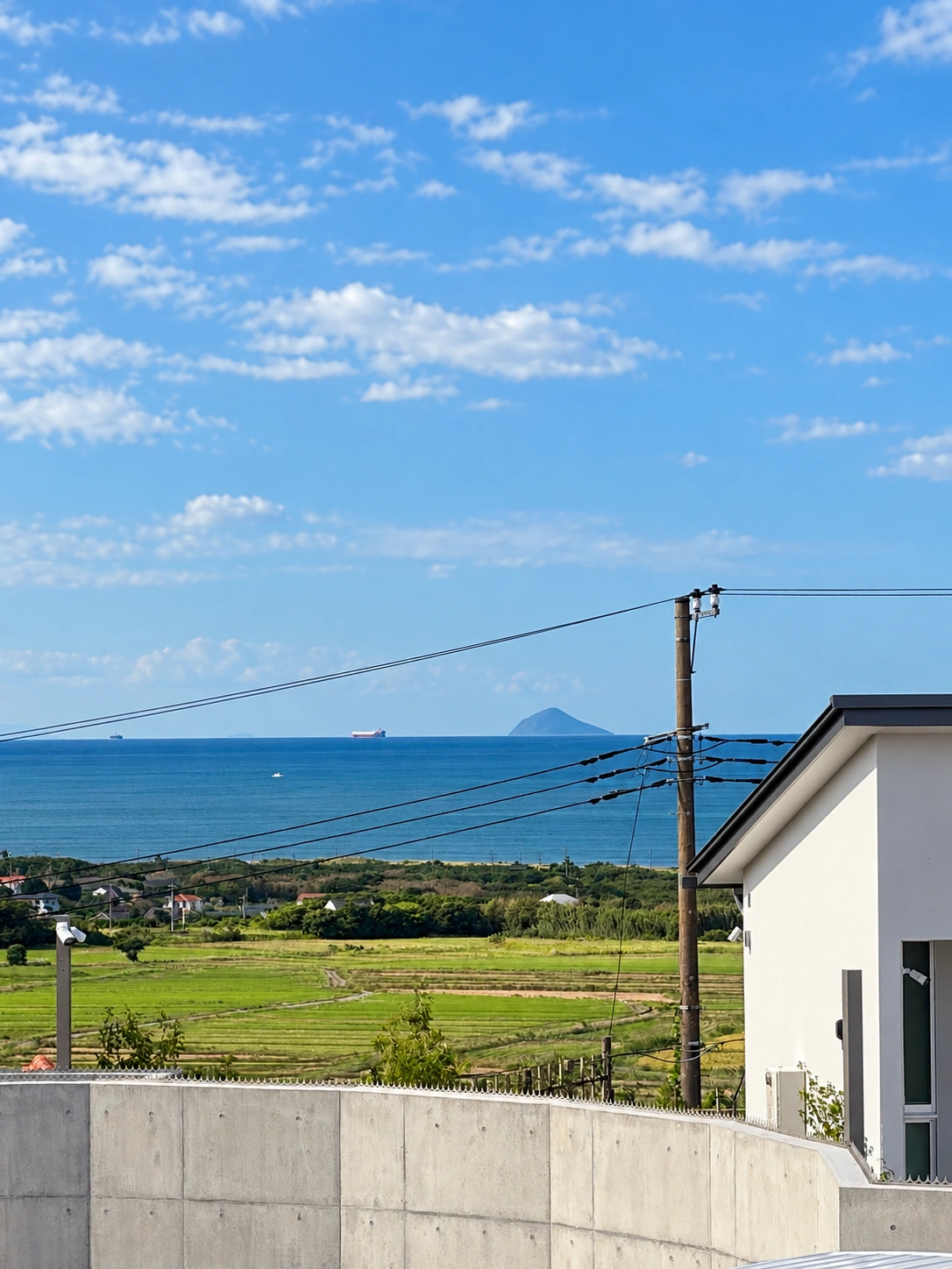 周辺の建物や電線越しに海が少し見える昼間の眺望